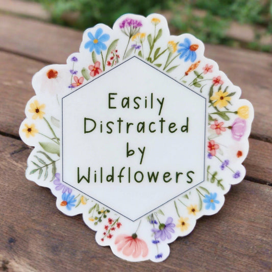 Easily distracted by wildflowers sticker on table background. wording is surrounded by hand drawn wildflowers. 